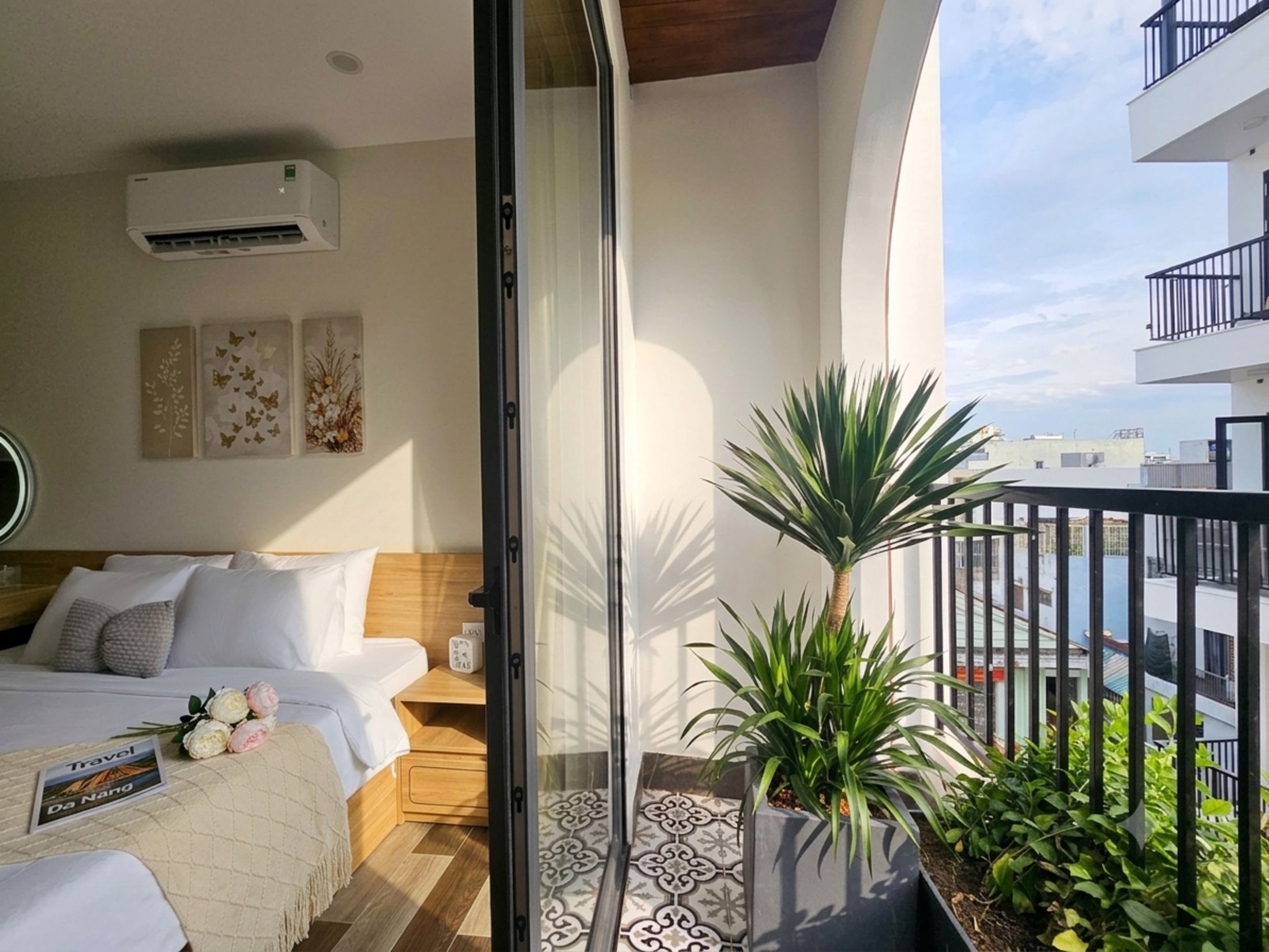 A hotel room with a bed, bedside table, and a potted plant.
