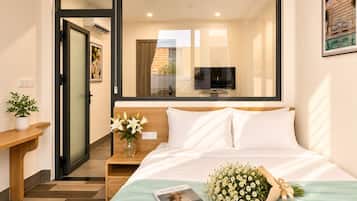 A hotel room with a bed, a bedside table with a vase of flowers, a framed picture on the wall, and a television mounted above the bed.
