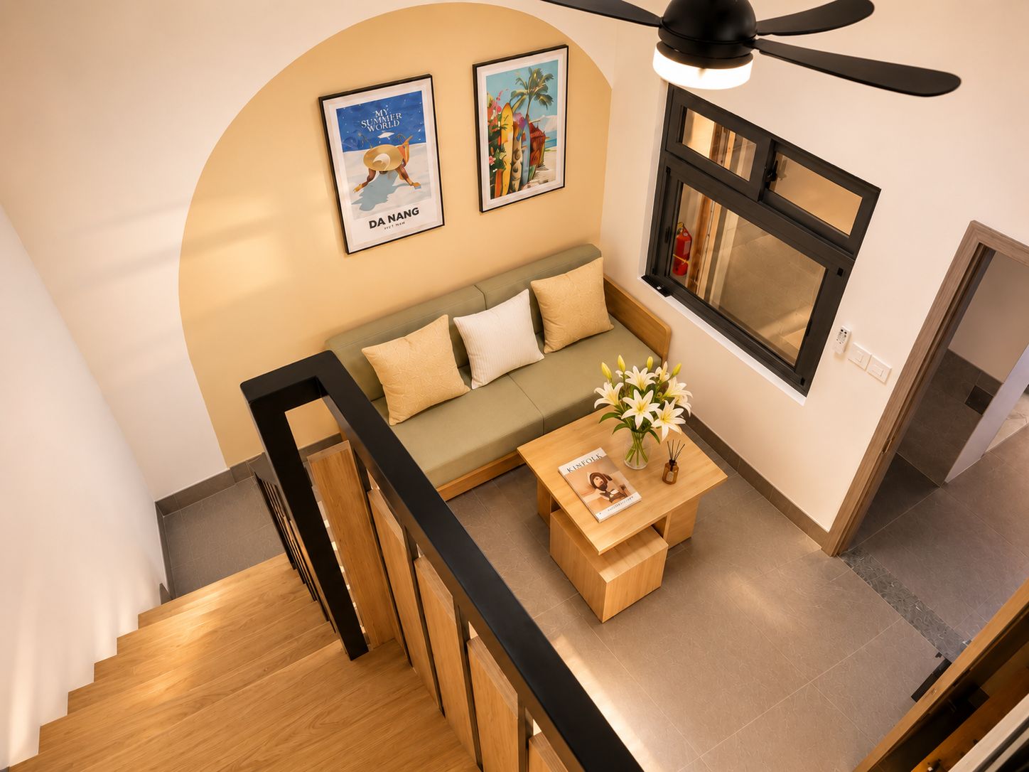 A modern living room with a wooden staircase, a sofa, a coffee table with flowers, and framed artwork on the wall.
