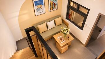 A modern living room with a wooden staircase, a sofa, a coffee table with flowers, and framed artwork on the wall.