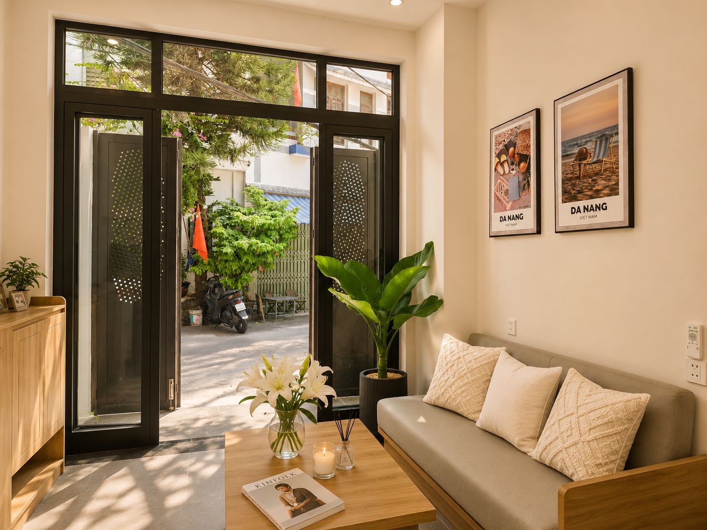 A modern living room with a sofa, a coffee table with a book and candles, and a large window with a view of the street.
