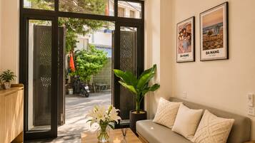 A modern living room with a sofa, a coffee table with a book and candles, and a large window with a view of the street.