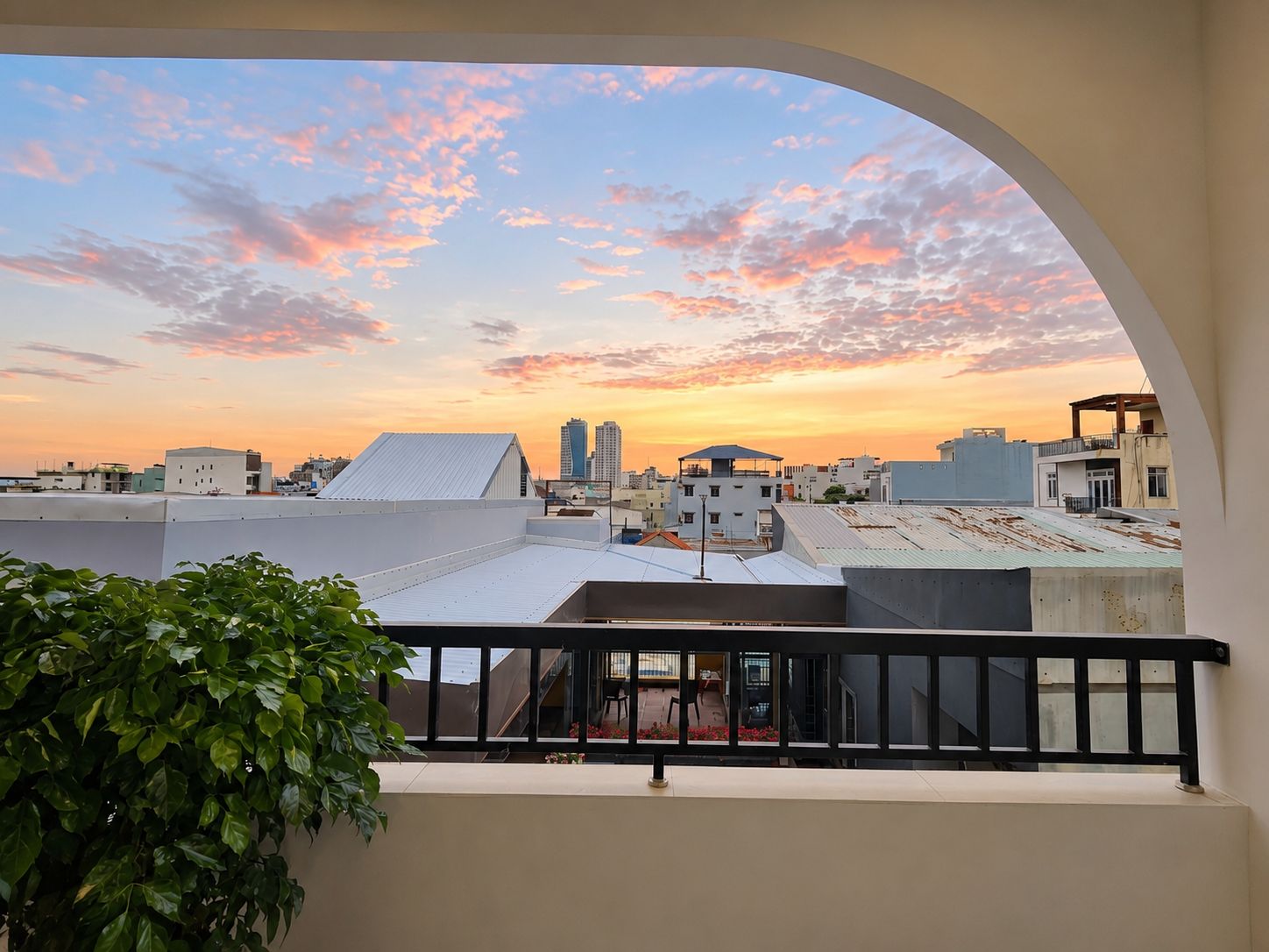 A balcony with a view of a cityscape at sunset, featuring buildings and a clear sky.