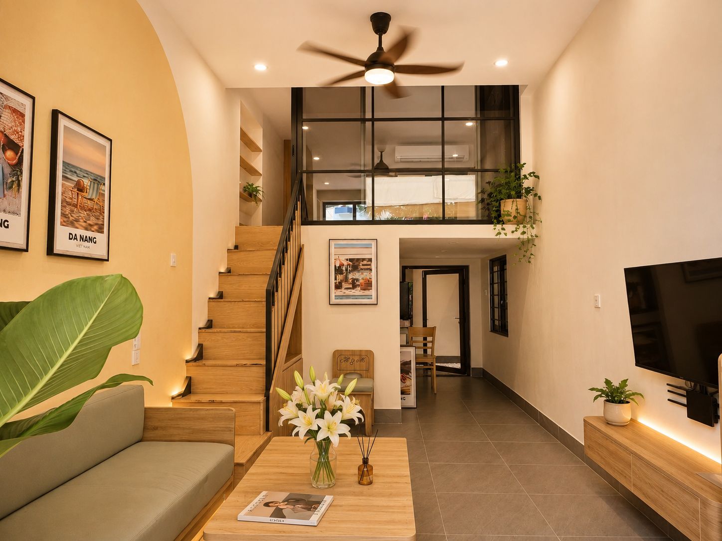 A modern living room with a staircase leading to an upper level, a flat-screen TV, and a large plant.