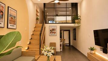 A modern living room with a staircase leading to an upper level, a flat-screen TV, and a large plant.