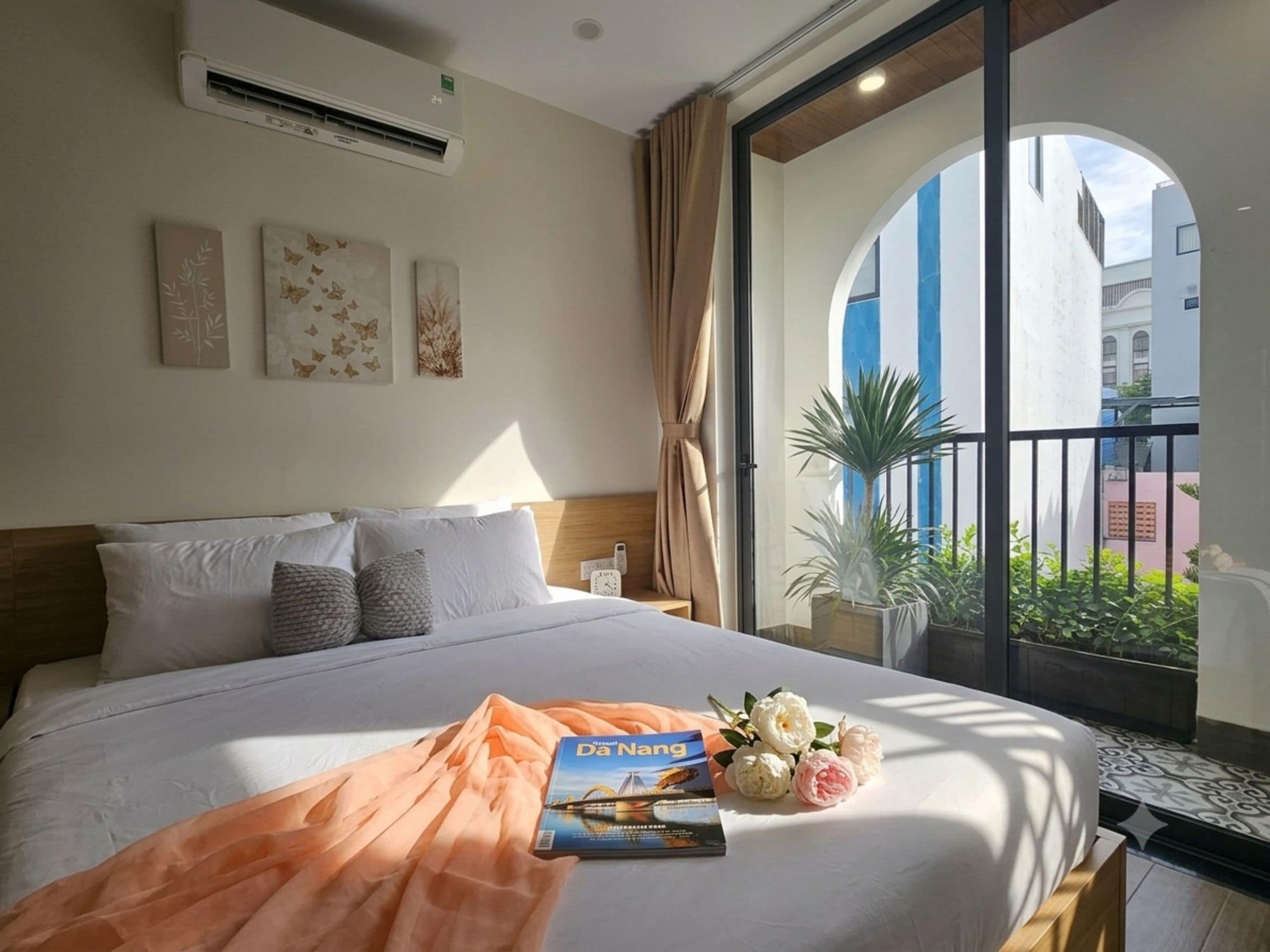 A hotel room with a large bed, a window with a view of buildings, and a plant on the windowsill.