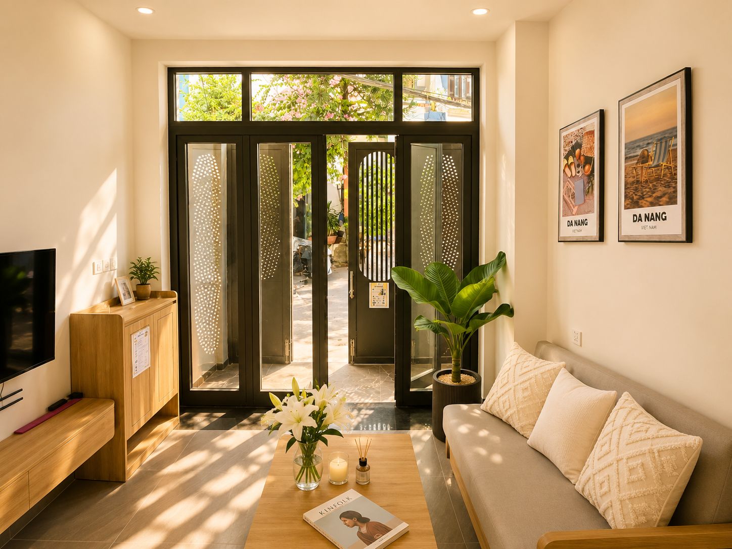 A modern living room with a sofa, coffee table, and a TV. There are two framed pictures on the wall and a door leading outside.