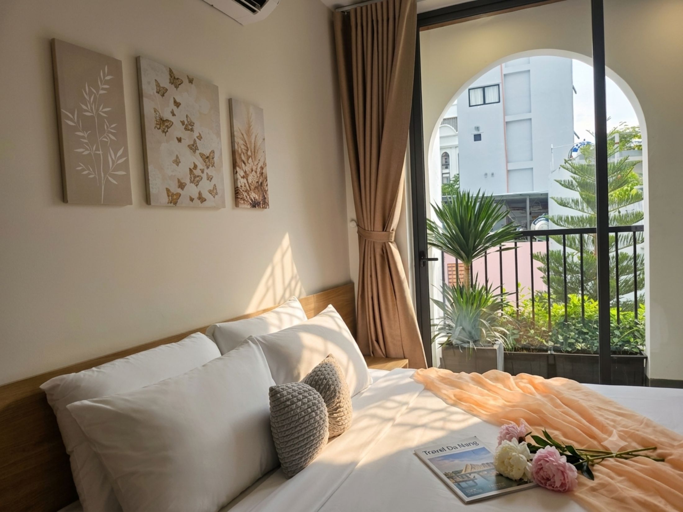 A hotel room with a bed, a window with a view of greenery, and three wall art pieces.
