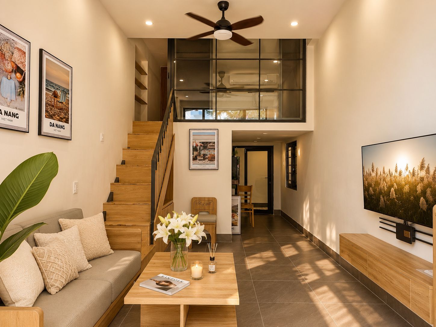 A modern living room with a staircase, a sofa, a coffee table with flowers, a TV, and framed pictures on the wall.
