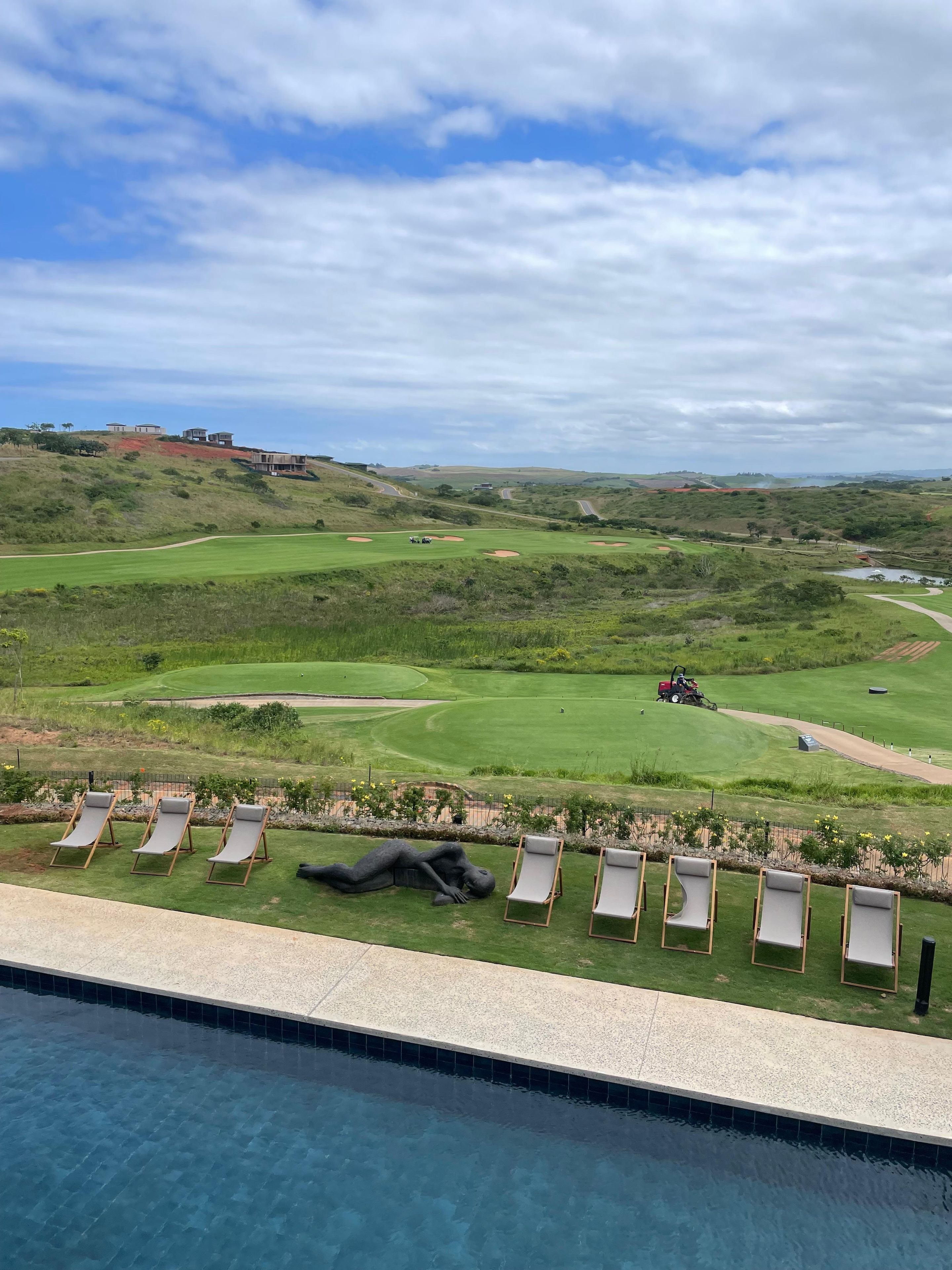 Vista della piscina con sedie a sdraio, un campo da golf sullo sfondo e cielo sereno.