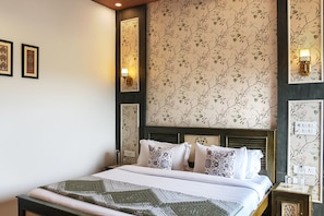 A neatly made bed with patterned bedding, a wall with floral wallpaper, and two wall-mounted light fixtures.