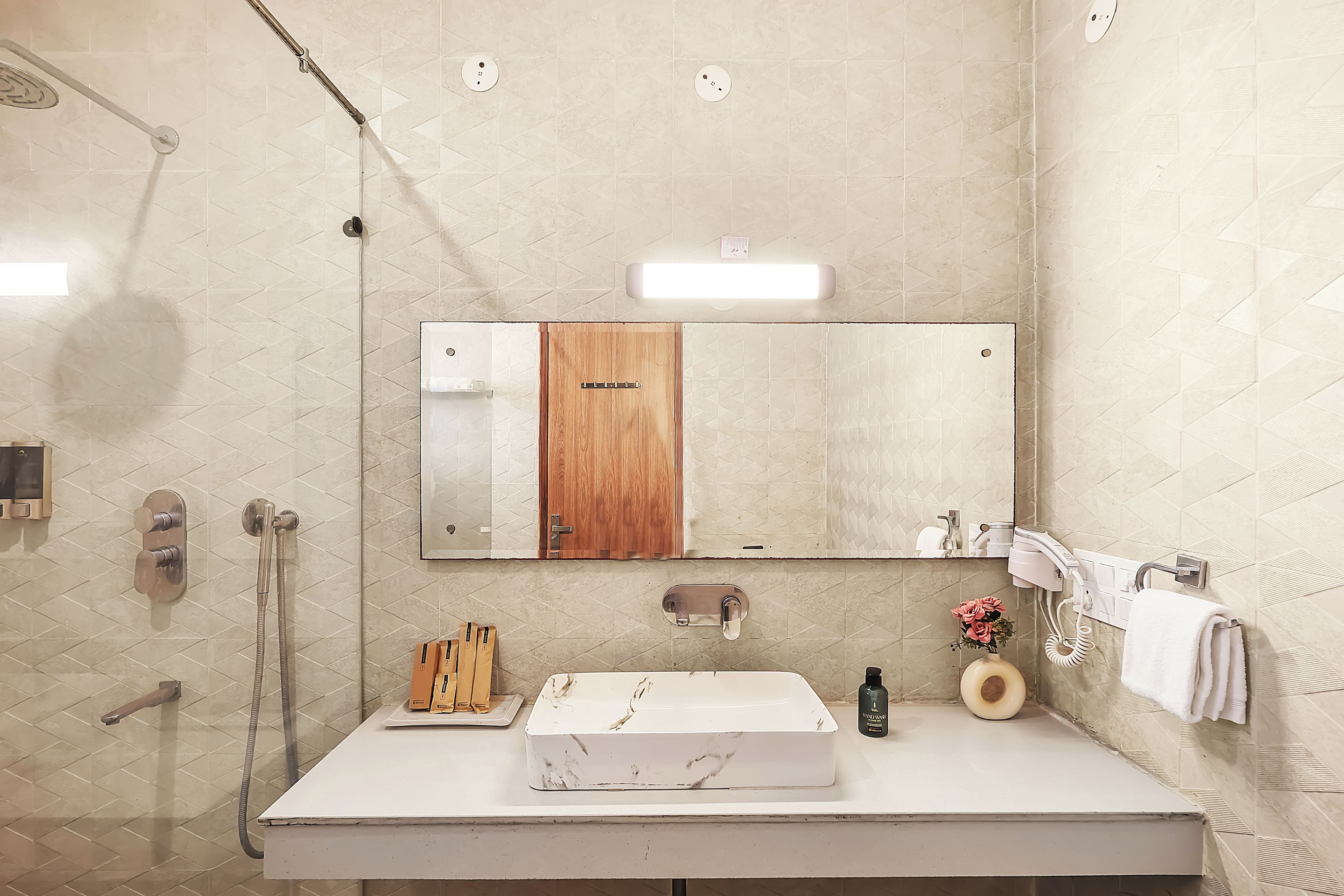 A bathroom with a white sink, a mirror, a wooden door, a towel rack, and a handheld showerhead.