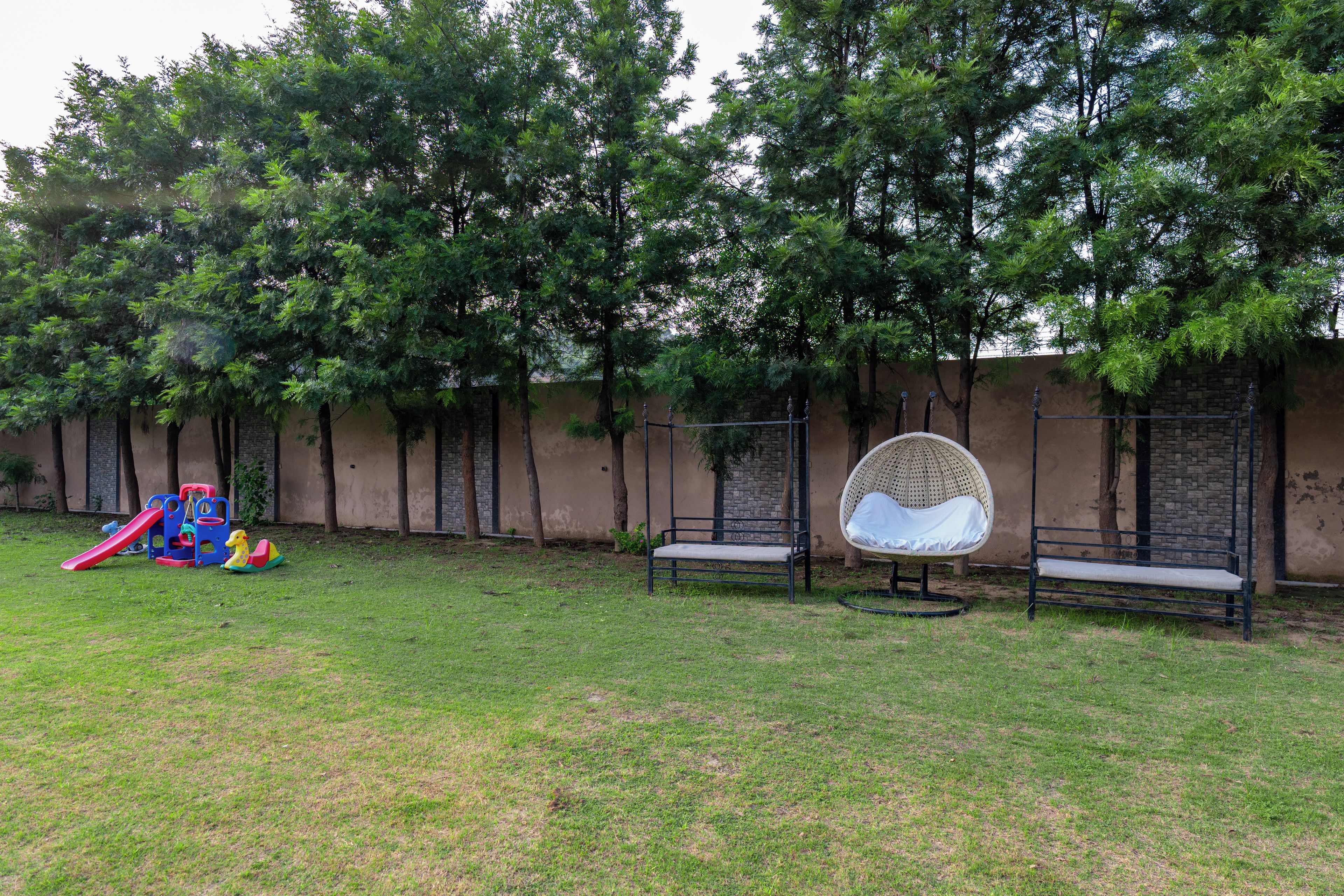 A grassy outdoor area with a children's playset, two benches, and a wall with trees.