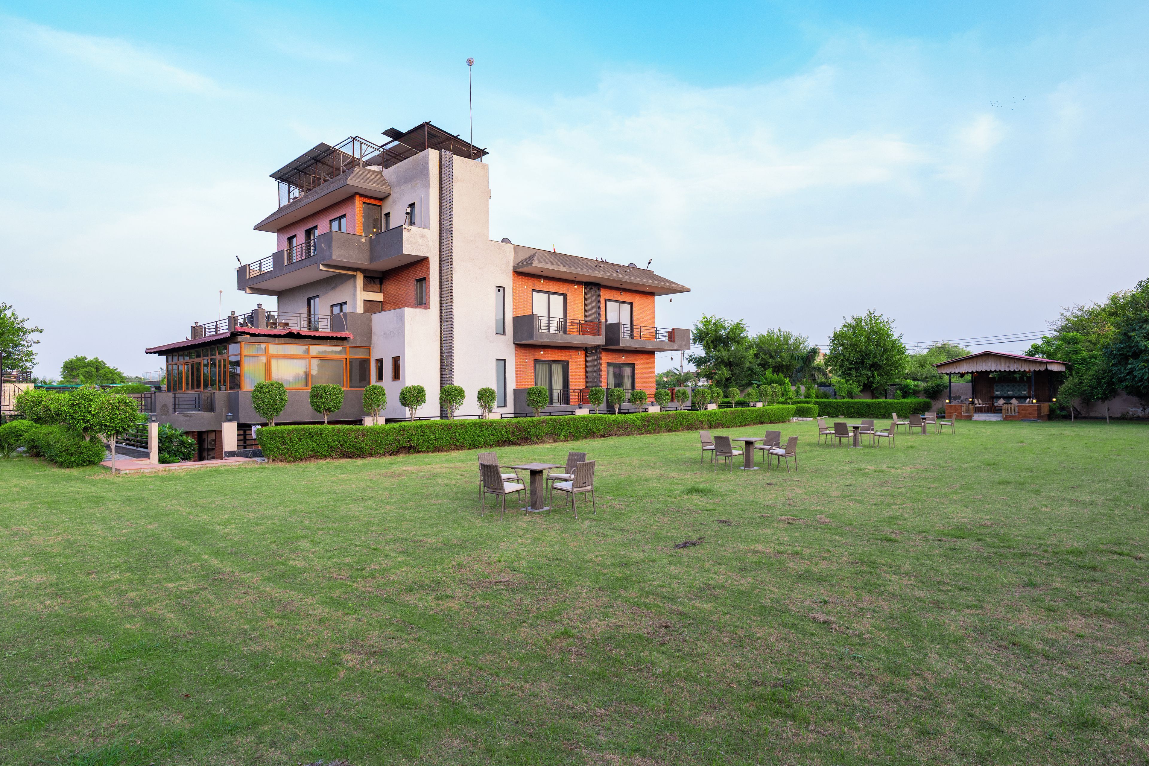 A multi-story residential building with a flat roof, a balcony, and a well-maintained lawn with outdoor seating.