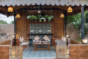 An outdoor seating area with wicker furniture and a central table, surrounded by a wooden fence and a bamboo roof structure.