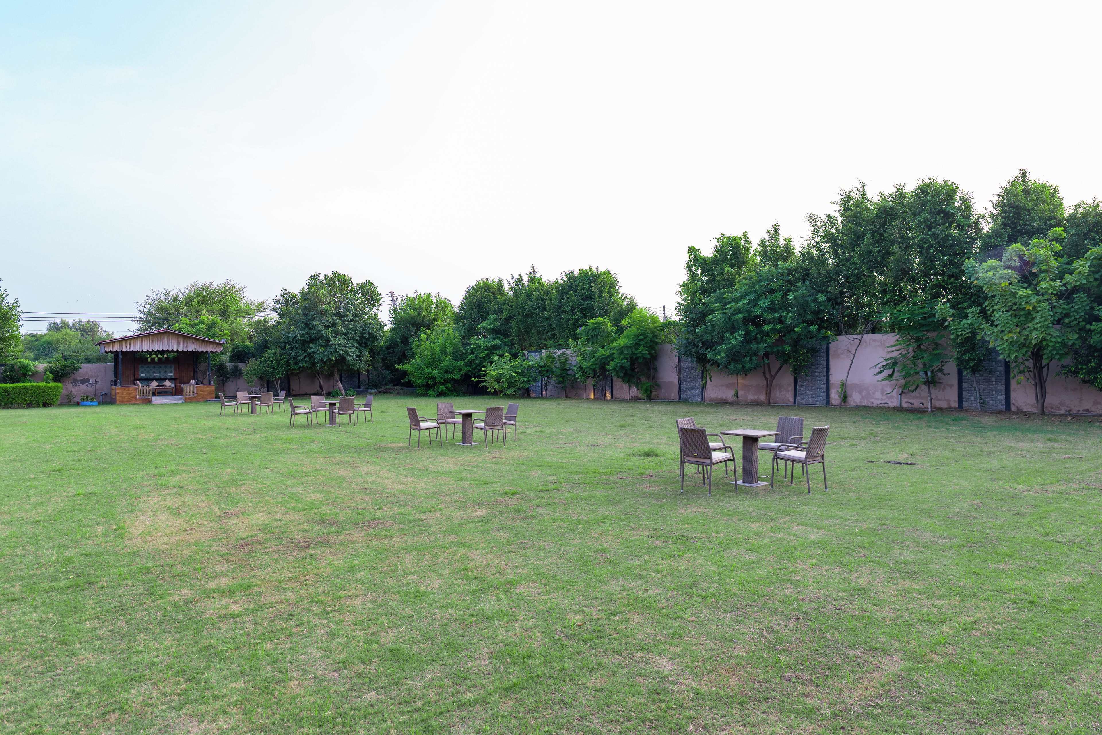 Een terras met tafels en stoelen, omringd door een gazon en bomen.