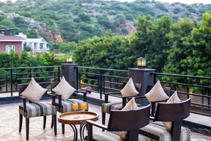 Une terrasse avec des sièges extérieurs, une table avec des verres de jus d’orange et une vue sur une colline.