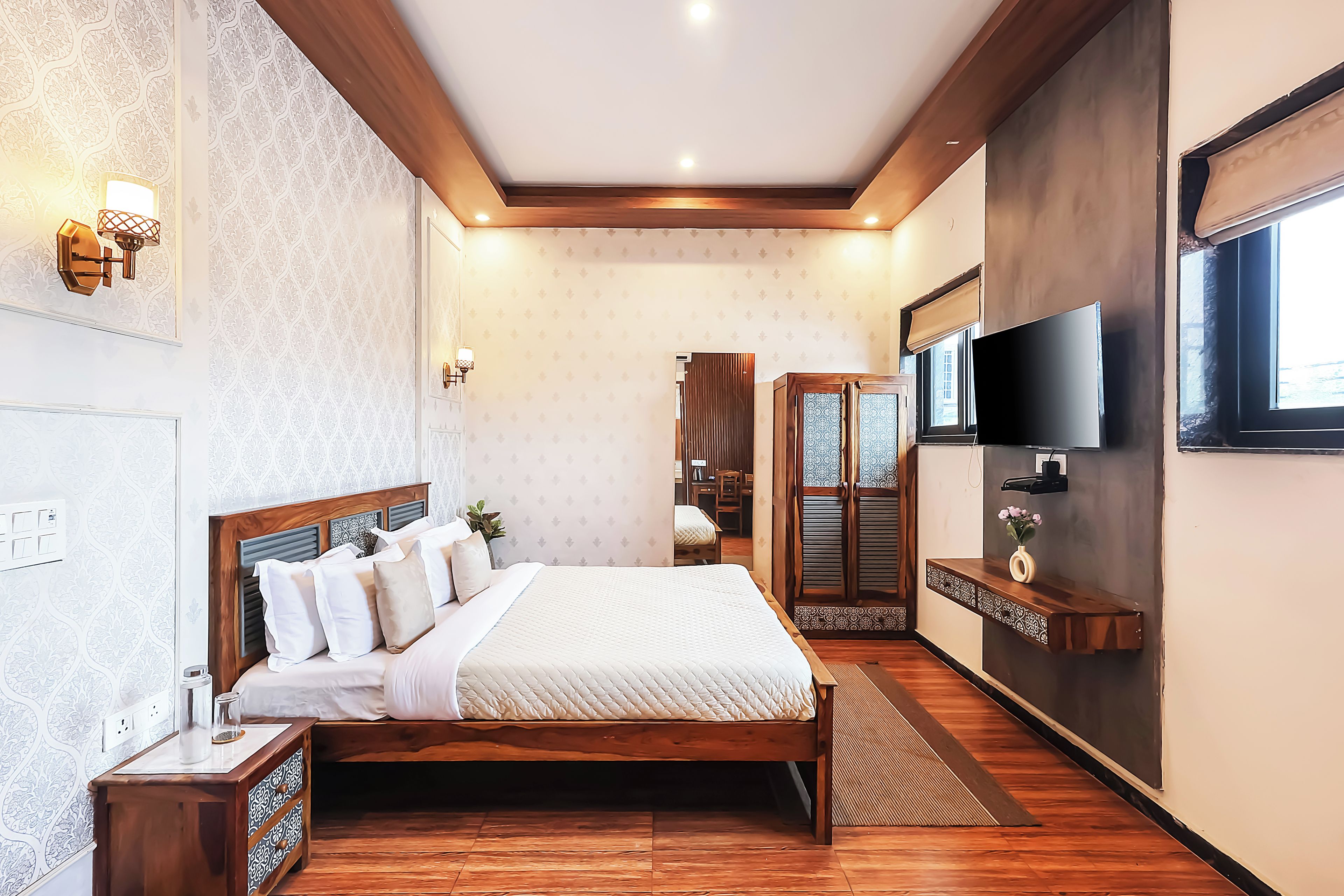 A bedroom with a wooden bed, bedside tables, a TV, and a patterned wall.