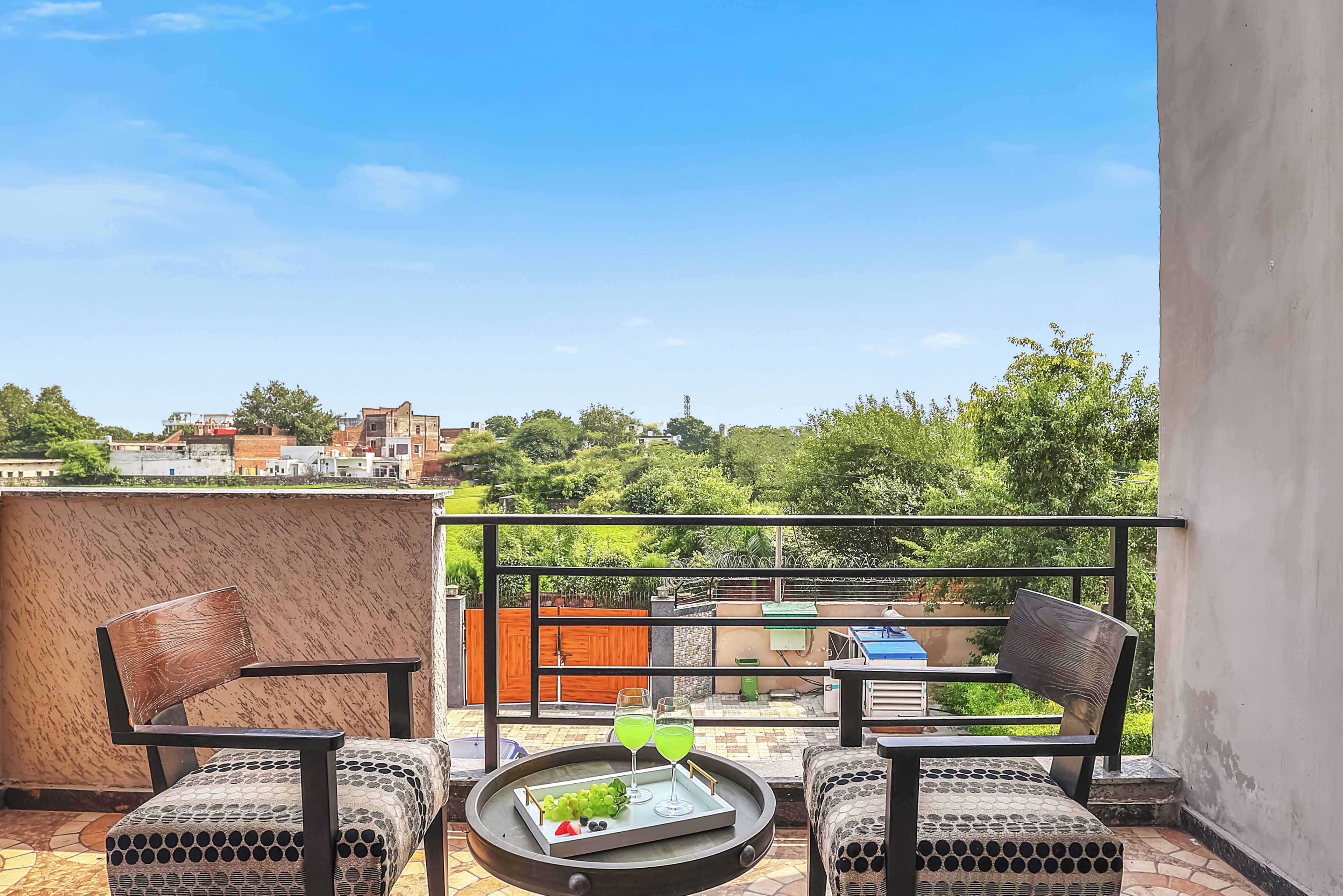 A balcony with two chairs, a small table with a tray of fruit and drinks, and a view of the cityscape.