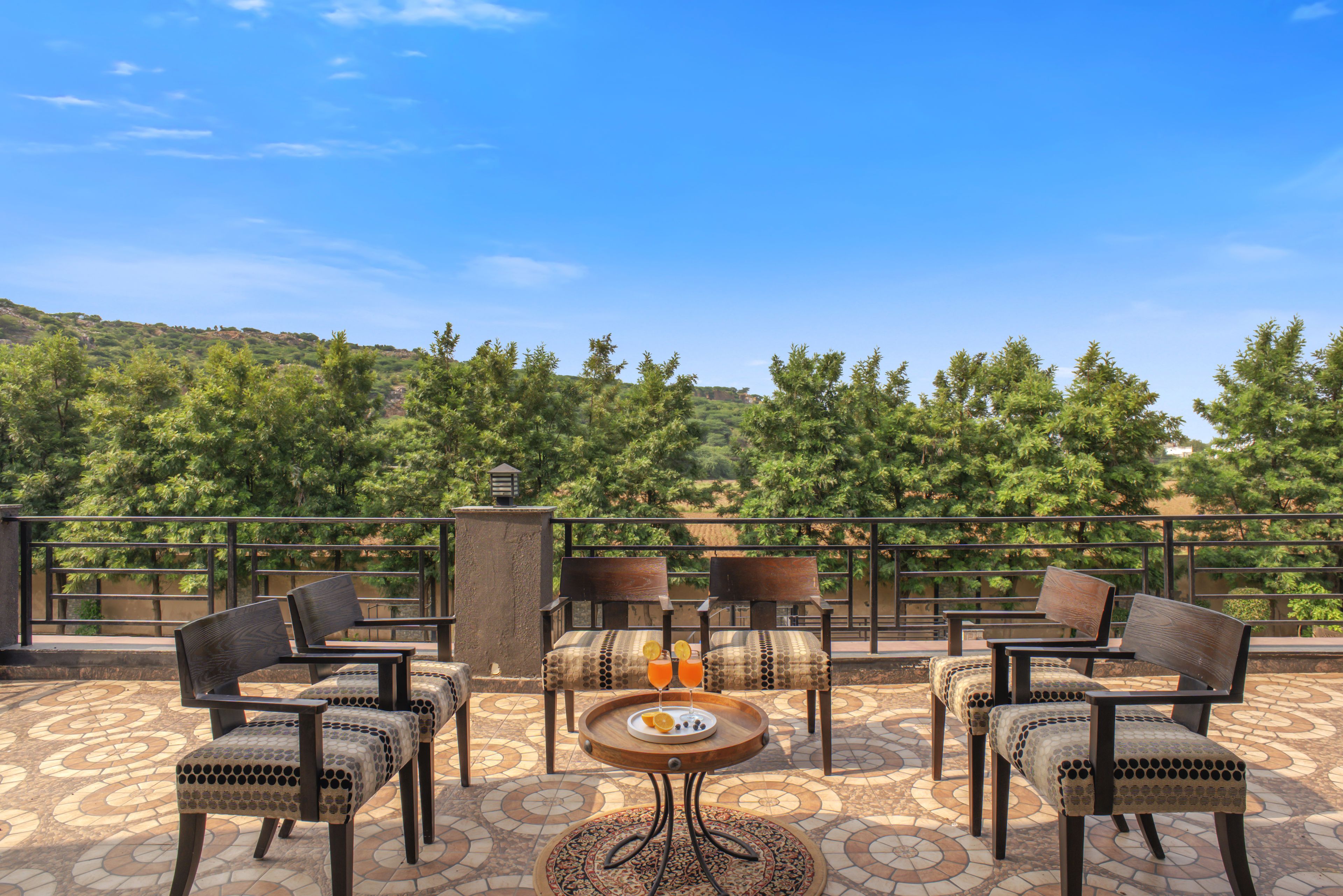 An outdoor seating area with a table and chairs, a patterned floor, and a view of a forested hillside.