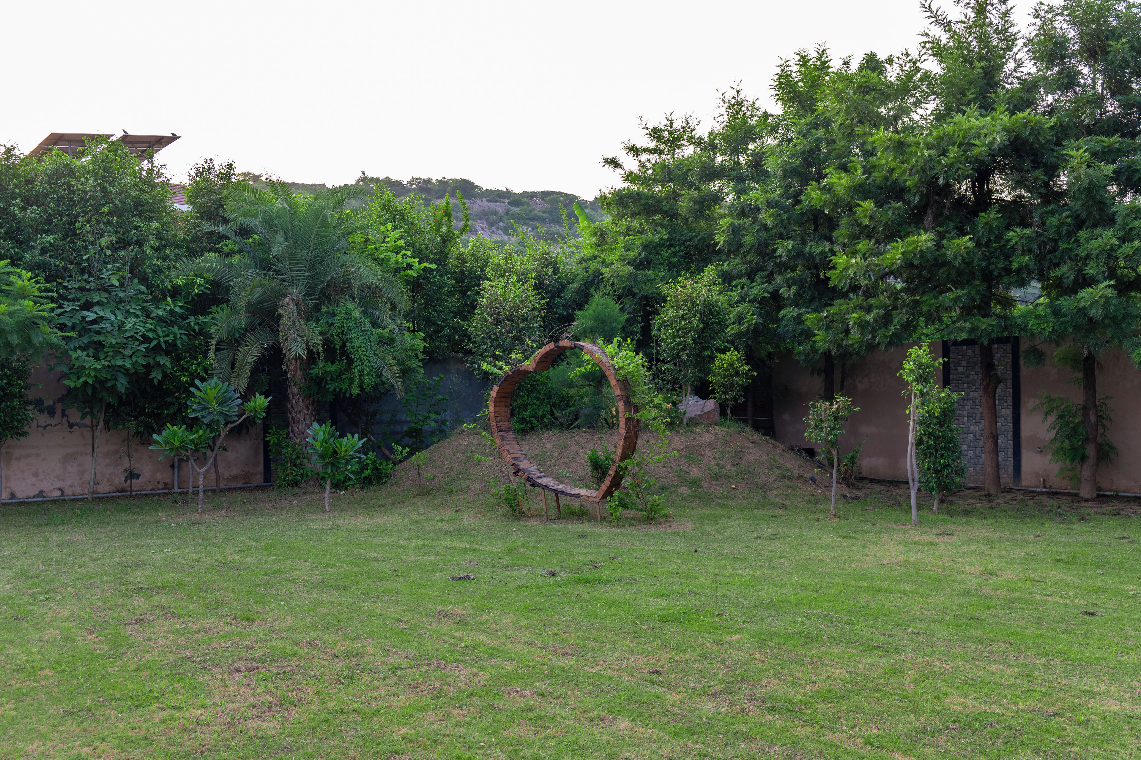 A circular brick structure in a grassy area with trees and a building in the background.