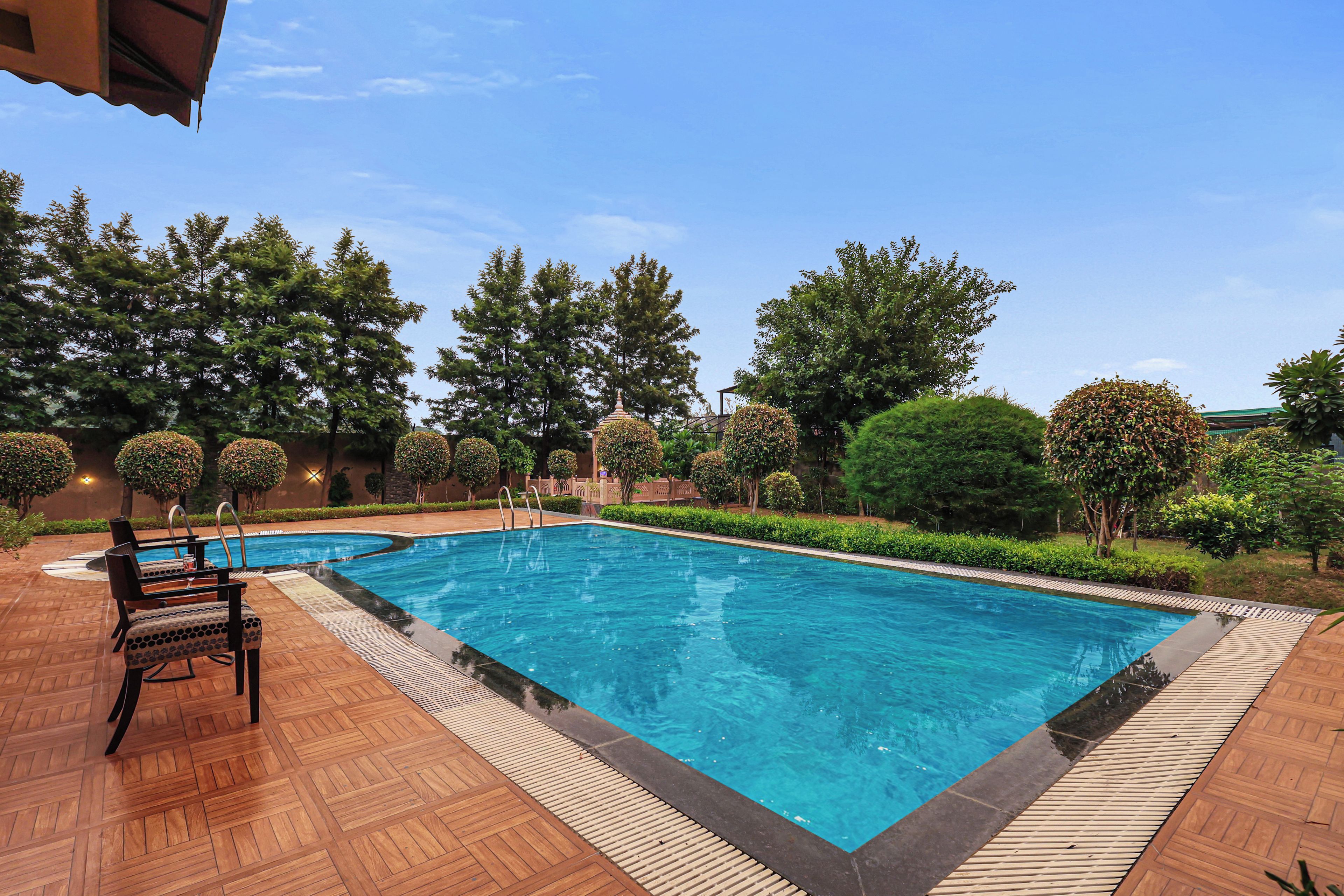 A rectangular swimming pool with a wooden deck surrounding it, equipped with a lounge area and a covered seating section.