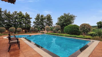 A rectangular swimming pool with a wooden deck surrounding it, equipped with a lounge area and a covered seating section.