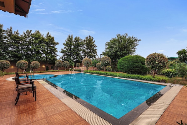 A rectangular swimming pool with a wooden deck surrounding it, equipped with a lounge area and a covered seating section.
