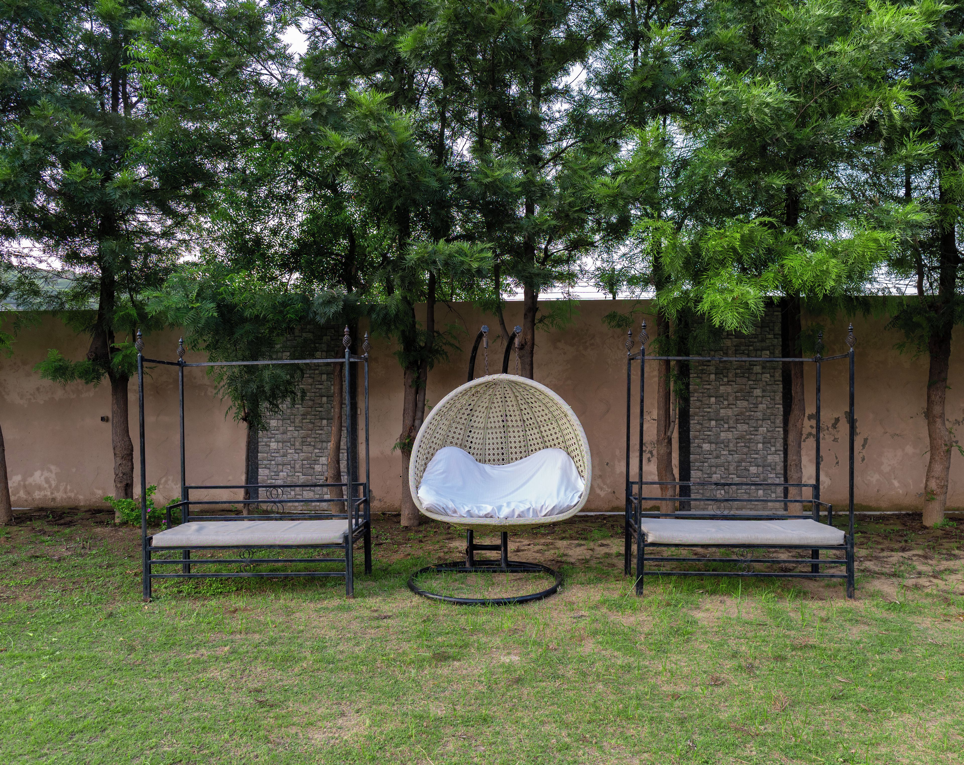 Two outdoor swing chairs with a woven seat and backrest, positioned on a grassy area with trees in the background.