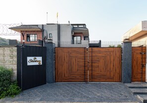 Une entrée fermée par un portail avec une pancarte, un bâtiment moderne doté d’un toit plat et un ciel dégagé.