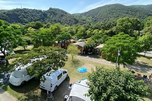 Ein Campingplatz mit Wohnmobilen, Zelten und einem kleinen Gebäude, umgeben von Bäumen und Hügeln.