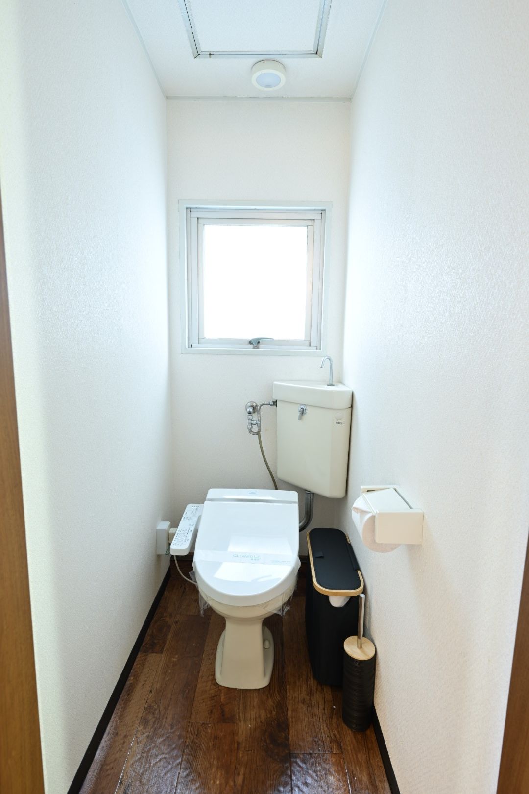 A small, narrow bathroom with a toilet, a window, and a white sink.