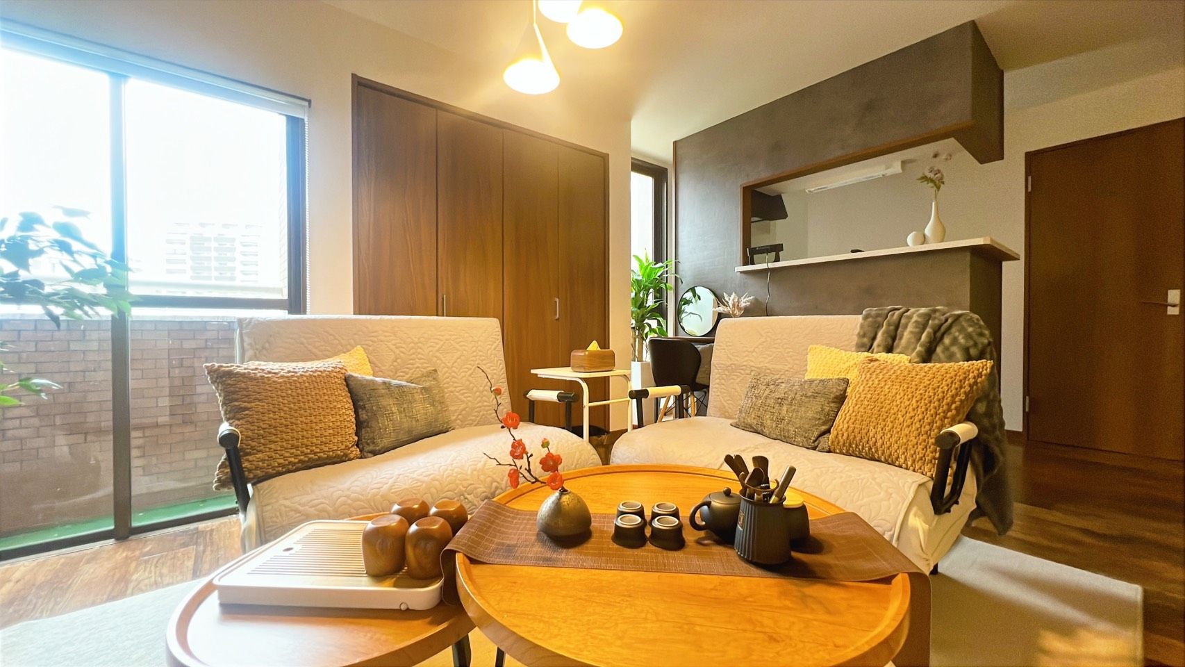 A modern living room with a sofa, a coffee table with tea set, and a large window providing natural light.
