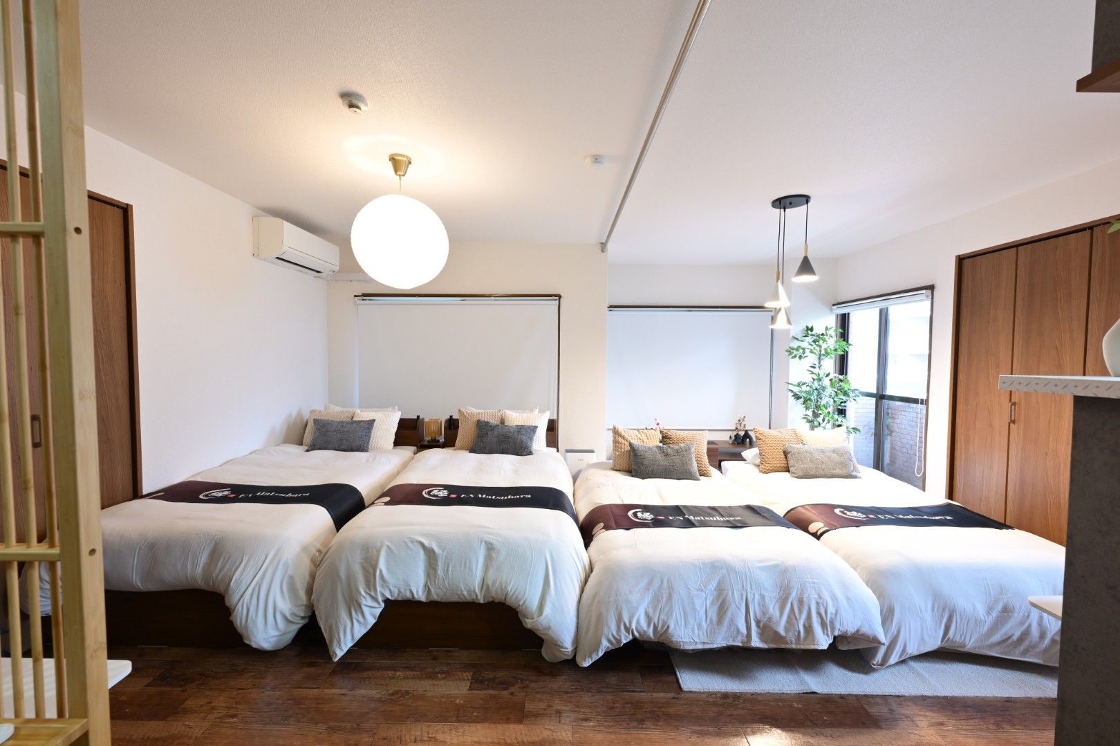 A hotel room with two beds, a large window, and a ceiling light.
