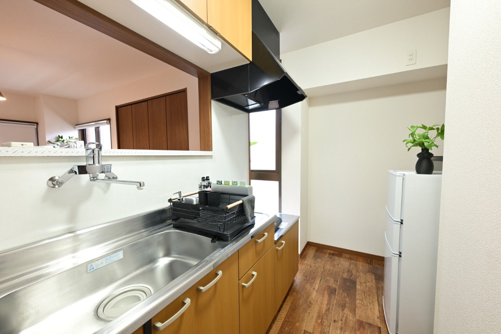 Una cocina con un lavaplatos de acero inoxidable, armarios de madera, una campana extractora negra y un refrigerador blanco.