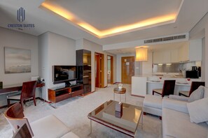 Ein modernes Hotelzimmer mit Flachbildfernseher, Essecke, Küche und Wohnbereich mit Sofa und Couchtisch.