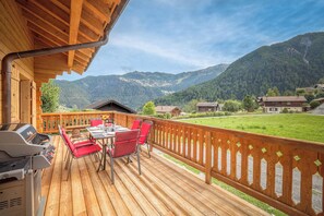 Een houten terras met een tafel en stoelen, uitkijkend op een bergachtig landschap.
