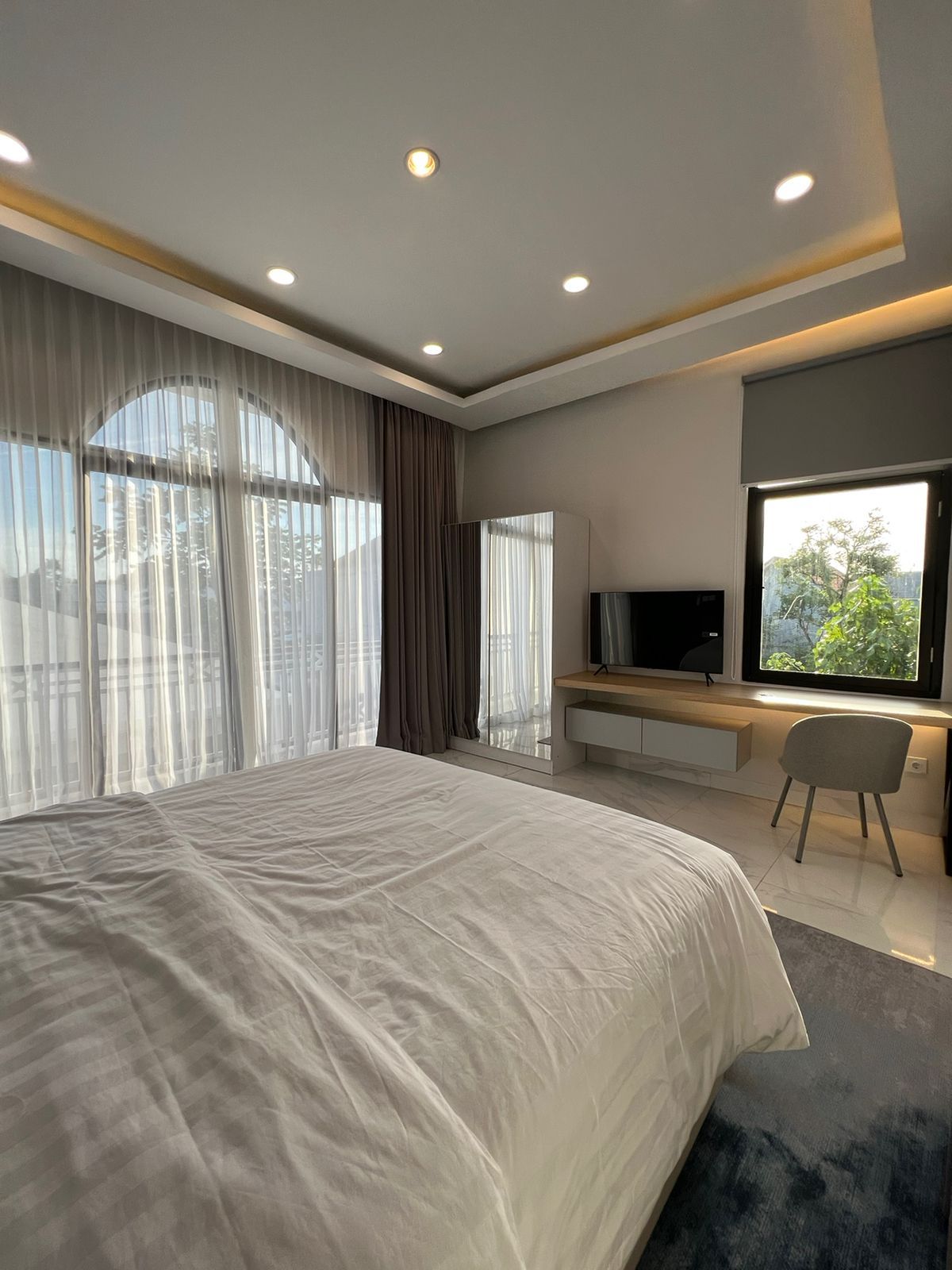 A modern bedroom with a large bed, a TV, and a desk area.