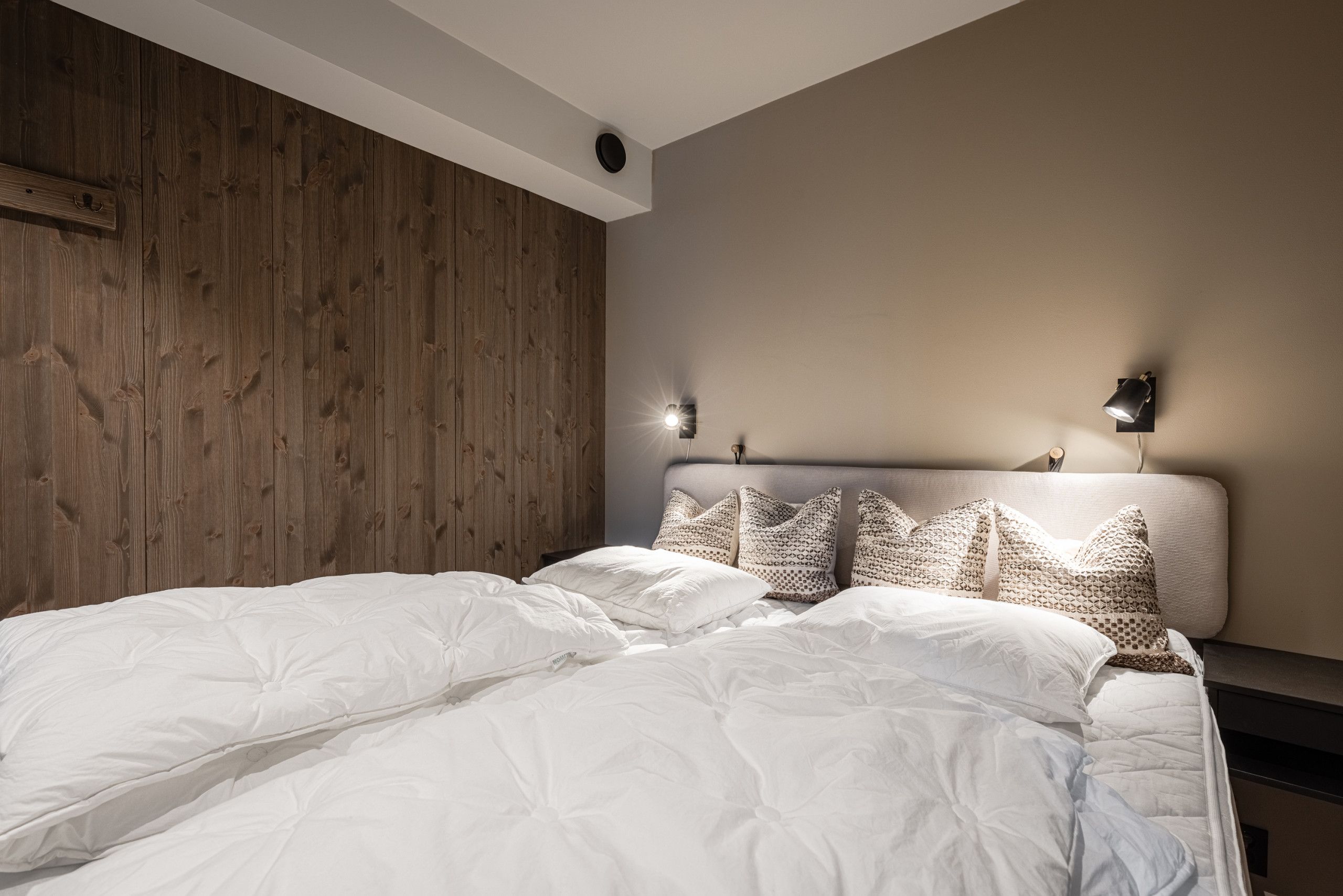 A bedroom with a wooden headboard, a bed with white bedding, and two wall-mounted reading lamps.