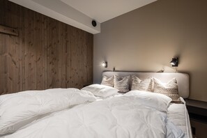 Une chambre à coucher avec une tête de lit en bois, un lit avec une literie blanche et deux lampes de lecture fixées au mur.