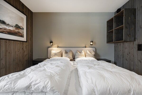 Un dormitorio con dos camas, cabeceros de madera, luces fijadas a la pared y un cuadro enmarcado.