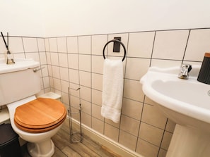 A bathroom with a toilet, a wooden toilet seat, a white sink, and a towel rack. - Eyrie Heights (Whitby)