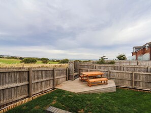 A wooden deck with a table and benches, surrounded by a wooden fence, overlooking a grassy field and distant hills. - Eyrie Heights (Whitby)