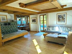 Un vaste espace de vie doté d’un plancher en bois, d’un canapé, d’une table à manger et d’une grande fenêtre qui laisse entrer la lumière naturelle.