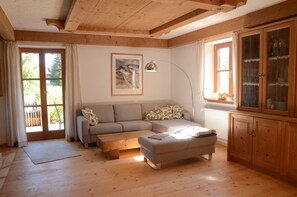A living room with a sofa, ottoman, wooden cabinet, and a painting on the wall. - Bergundmoos, Allgäu - A Vacation Home for the Whole Family (Pfronten)