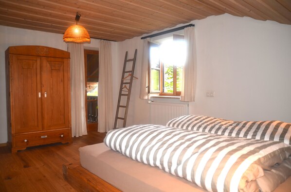 Une chambre avec une armoire en bois, un lit avec une literie à rayures, un luminaire suspendu et une fenêtre avec des rideaux.