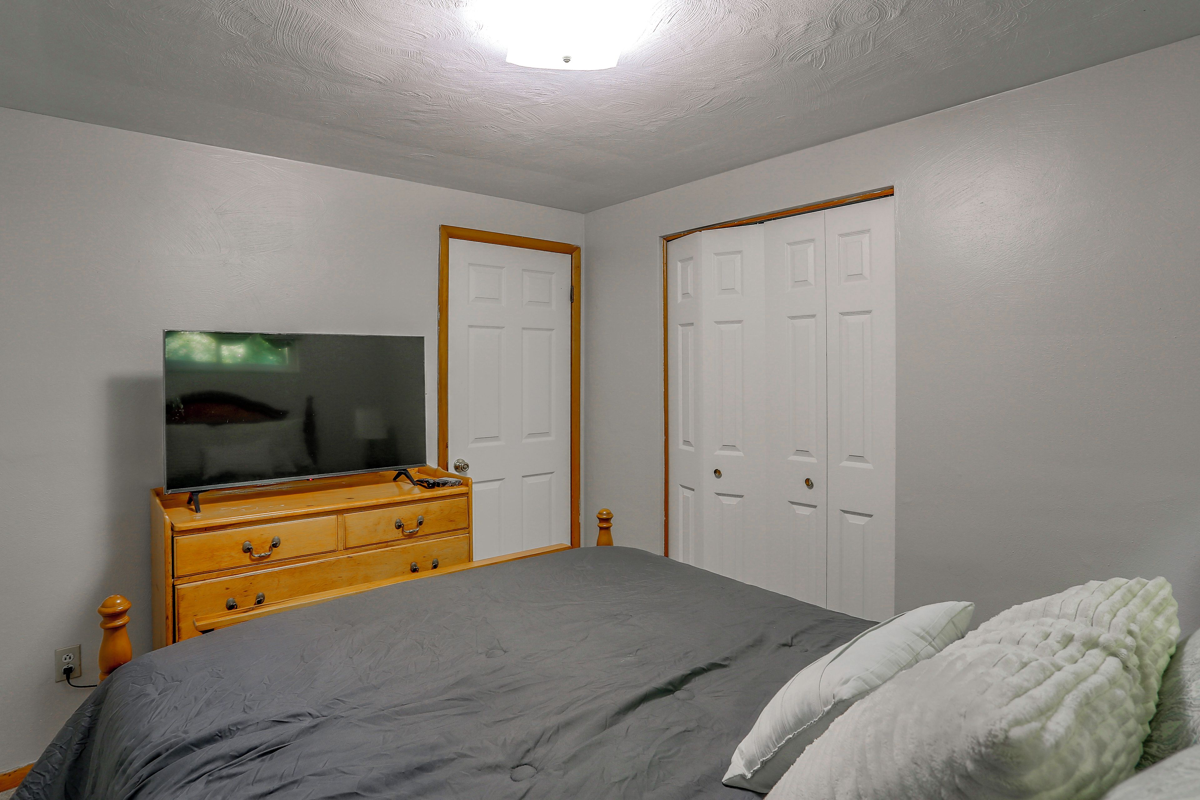 A bedroom with a bed, dresser, television, and two doors.