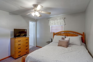 A bedroom with a bed, a dresser, a ceiling fan, a window with curtains, and a door.