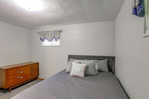 A bedroom with a bed, a wooden dresser, and a window with curtains.