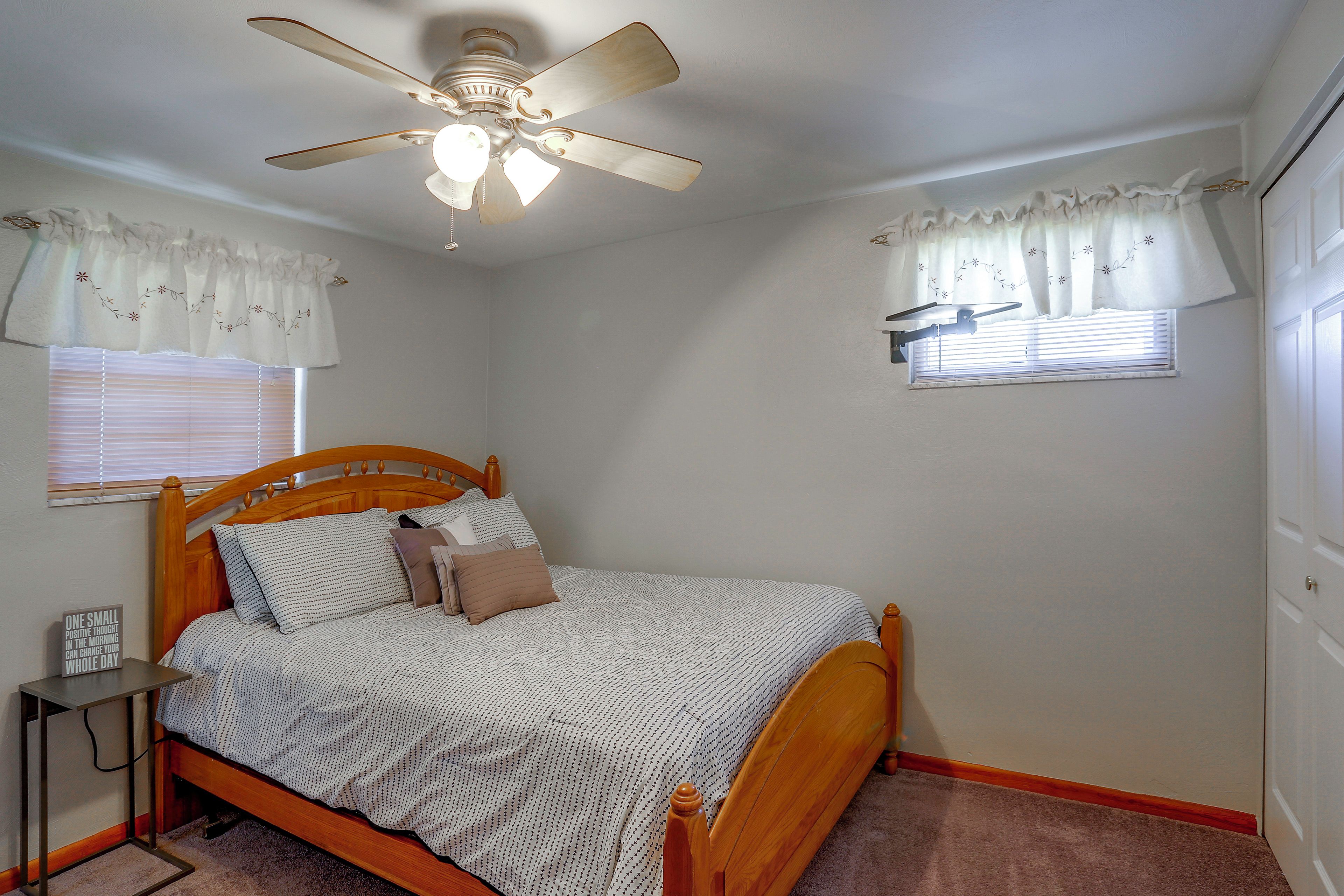 A bedroom with a wooden bed, a ceiling fan, and two windows with curtains.